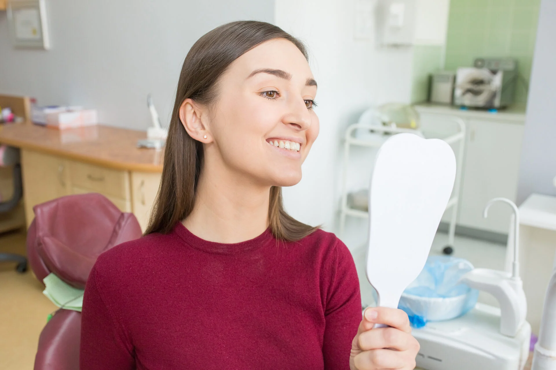 Young woman sits in a dental chair looking in mirror as a patient.
