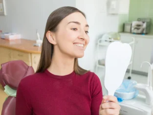 Young woman sits in a dental chair looking in mirror as a patient.